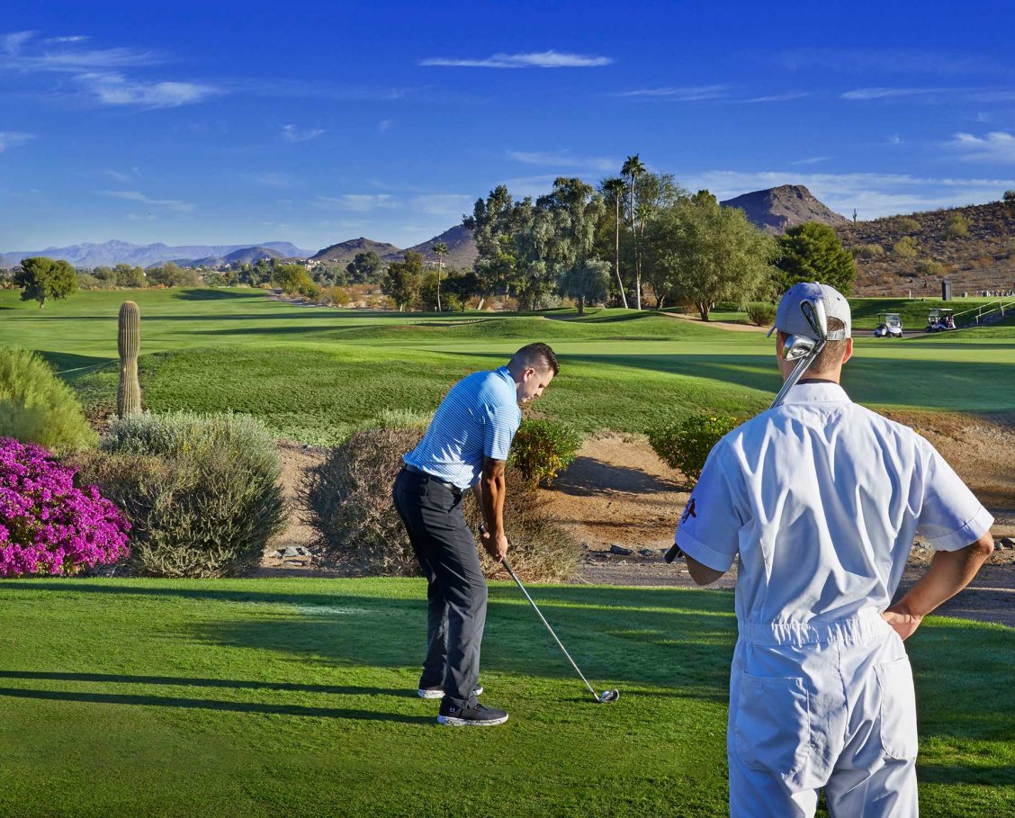 Golfer and caddie on fairway teeing off