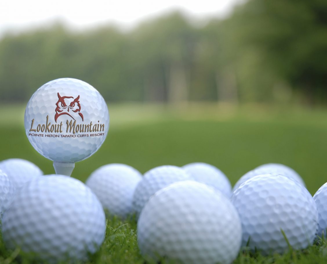 Golf Balls_Logo2 Golf balls on grass with one on a tee with Lookout Mountain Golf Course logo on it