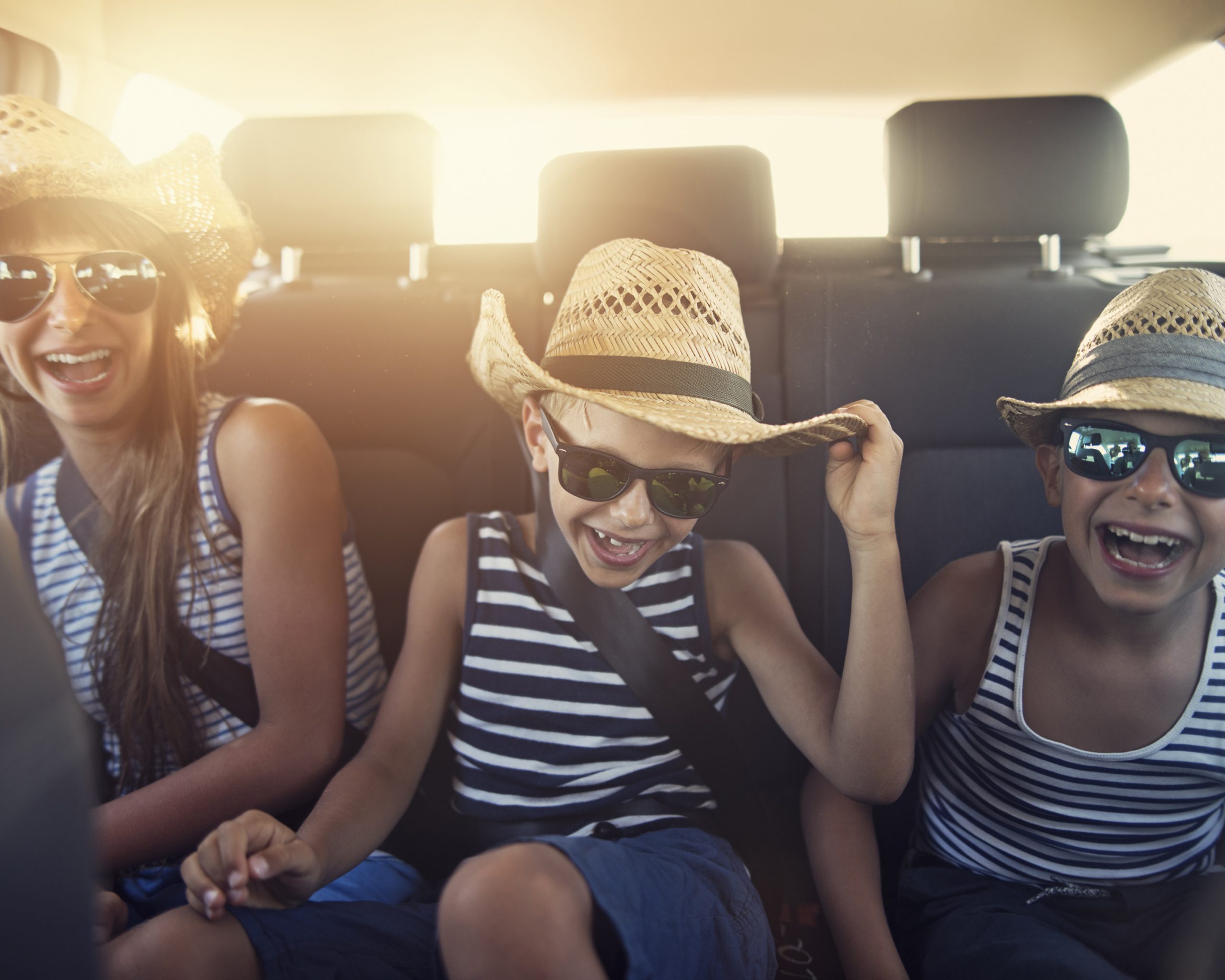 Kids in the back seat of a car enjoying a road trip on sunny day