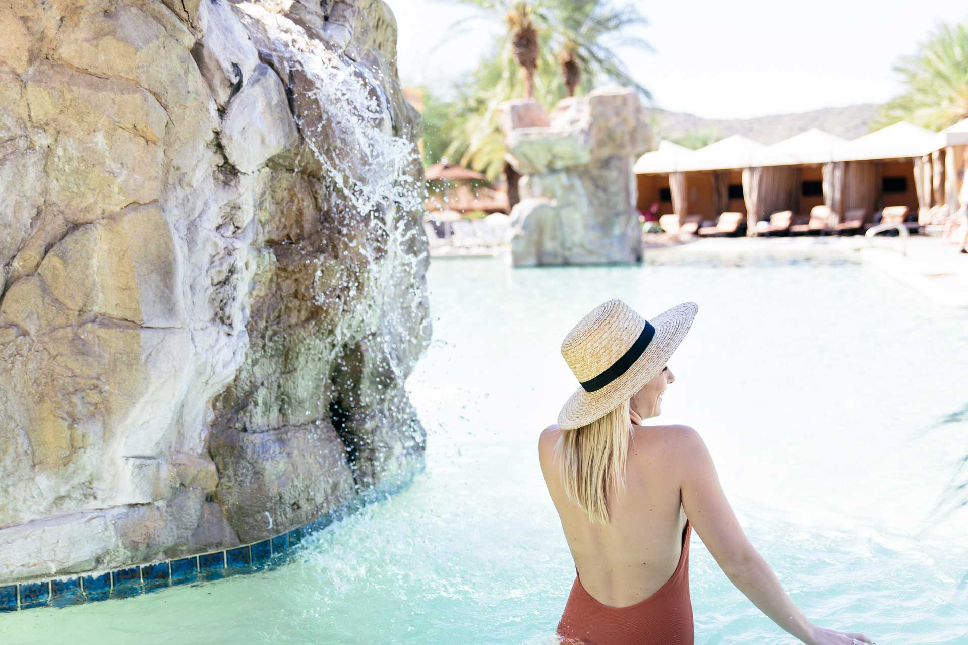 Woman wading in the pool next to a rock waterfall