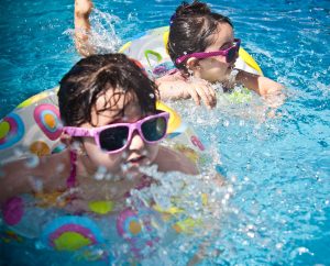 Two young children with sunglasses on splashing and playing in the pool with inflatable water toys